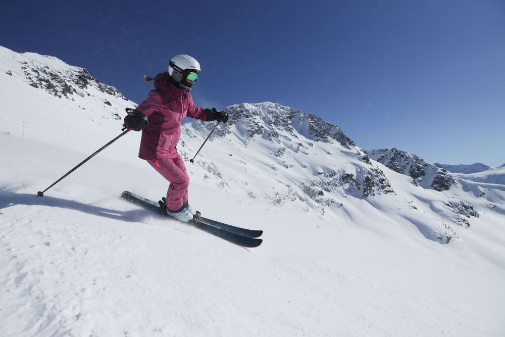 Skier in pink jacket gliding down snowy mountain slope on sunny day.
Whistler Blackcomb