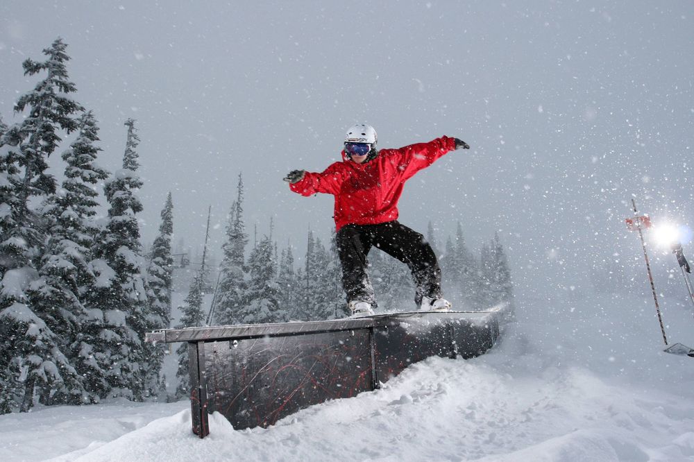 Snowboarder in red jacket performing jump trick over rail in snowy conditions.
Whistler Blackcomb
