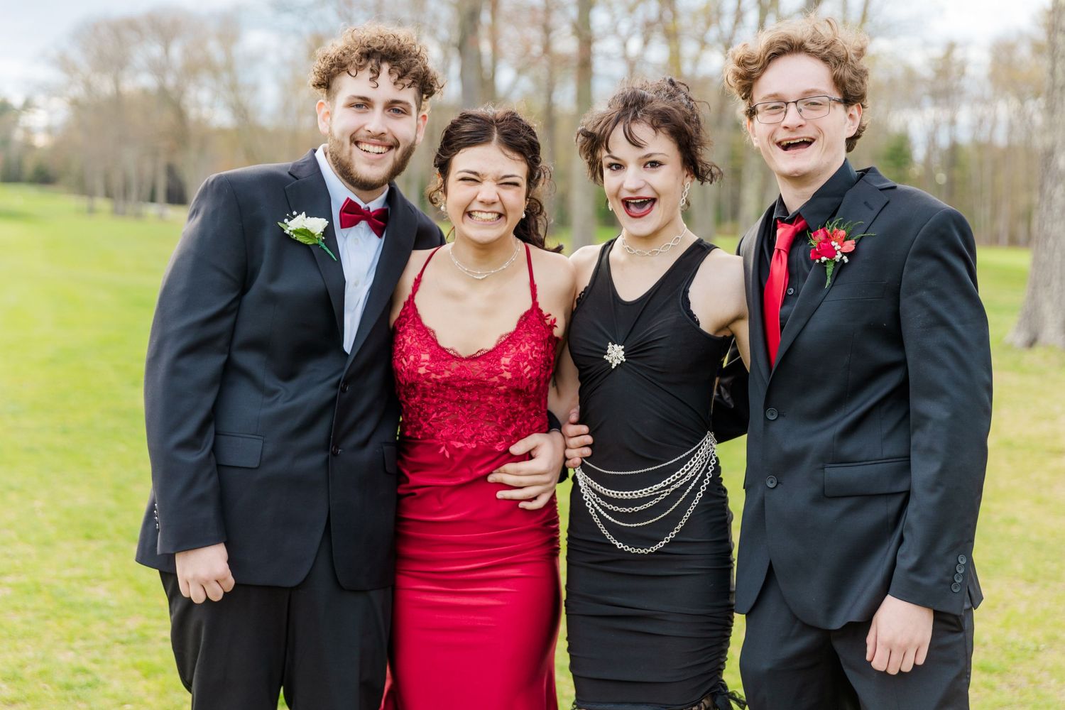 Four people in formal wear smile for a photo outdoors during a special occasion.