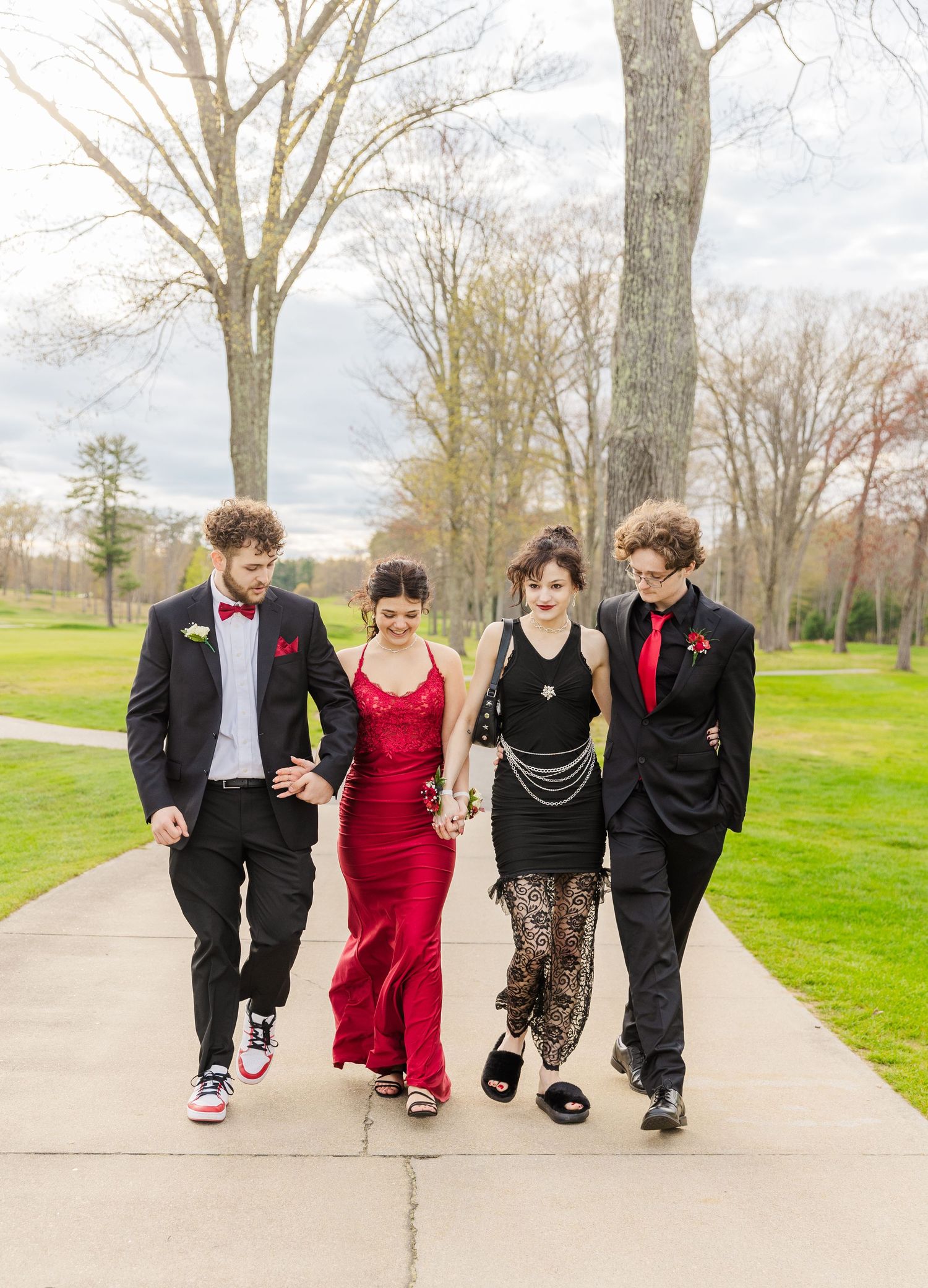 Four friends walk together on a pathway wearing formal attire for a special event.