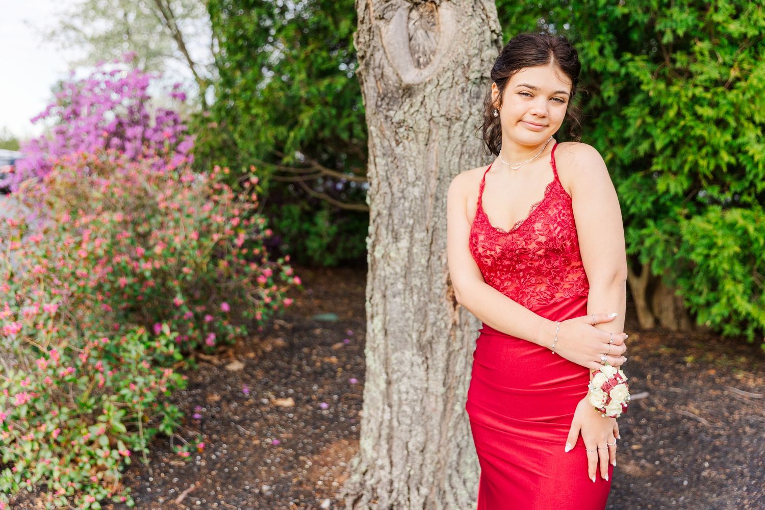 A person in a red sequined dress poses elegantly against a tree with spring blossoms in background.