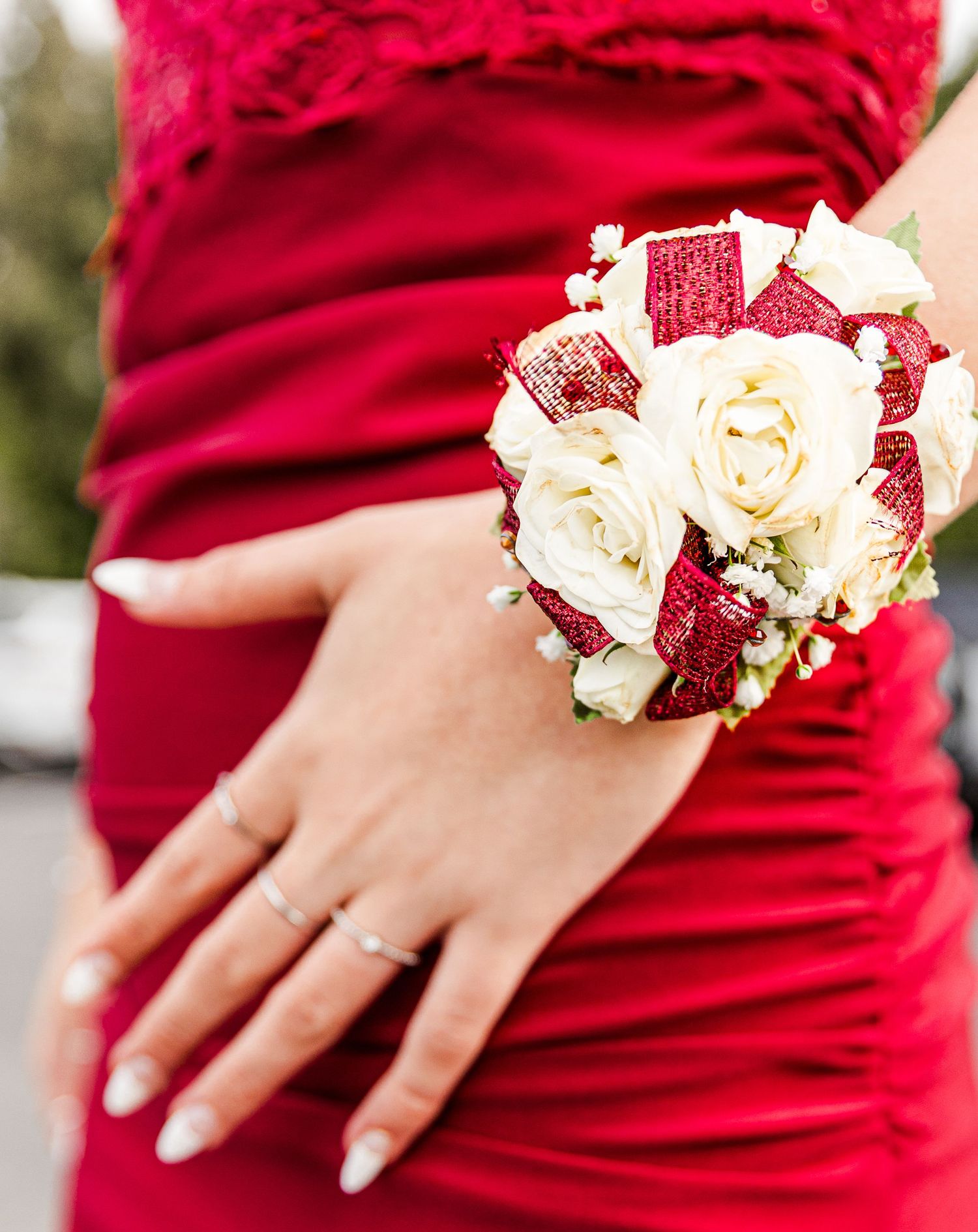 A white rose and red fabric corsage adorns the wrist of someone wearing a red dress.