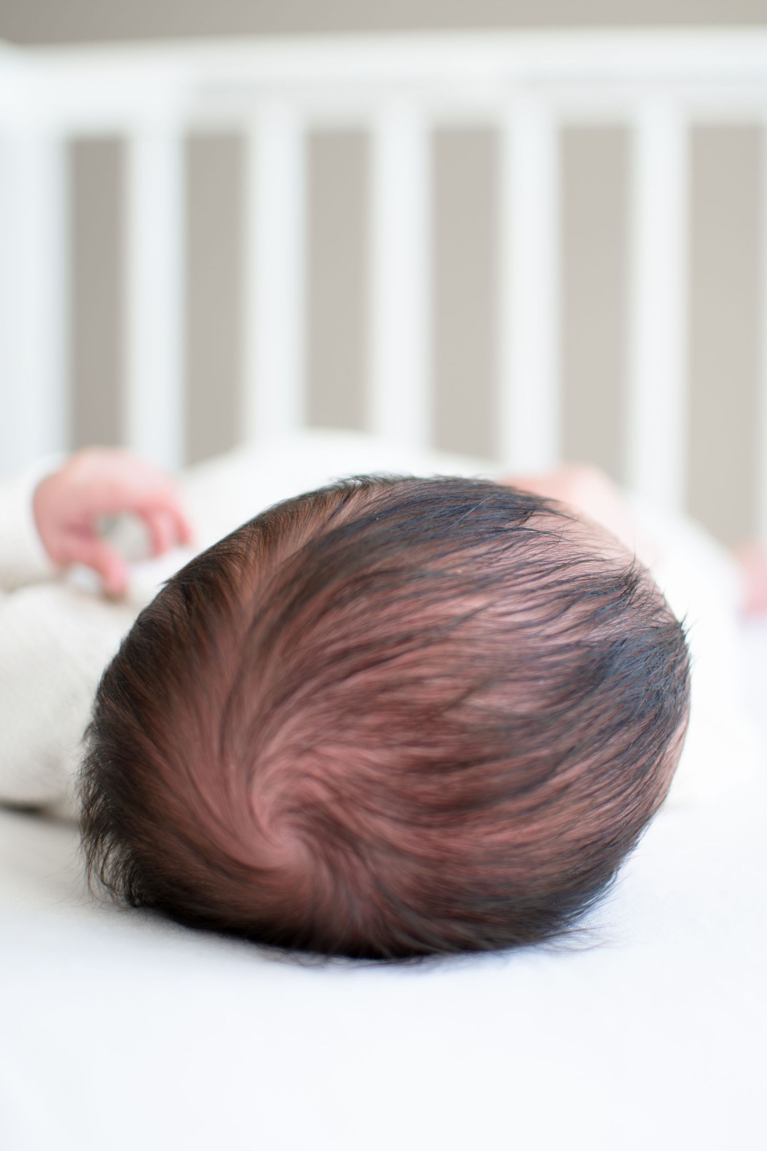 Baby girl has a head full of dark hair as she sleeps in her crib in her home.