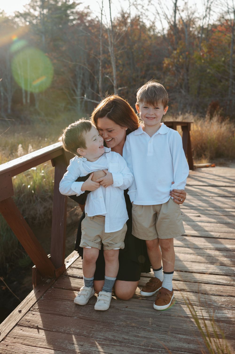 Two children sitting together on a wooden bridge share sweet moments in matching white shirts and khaki shorts.