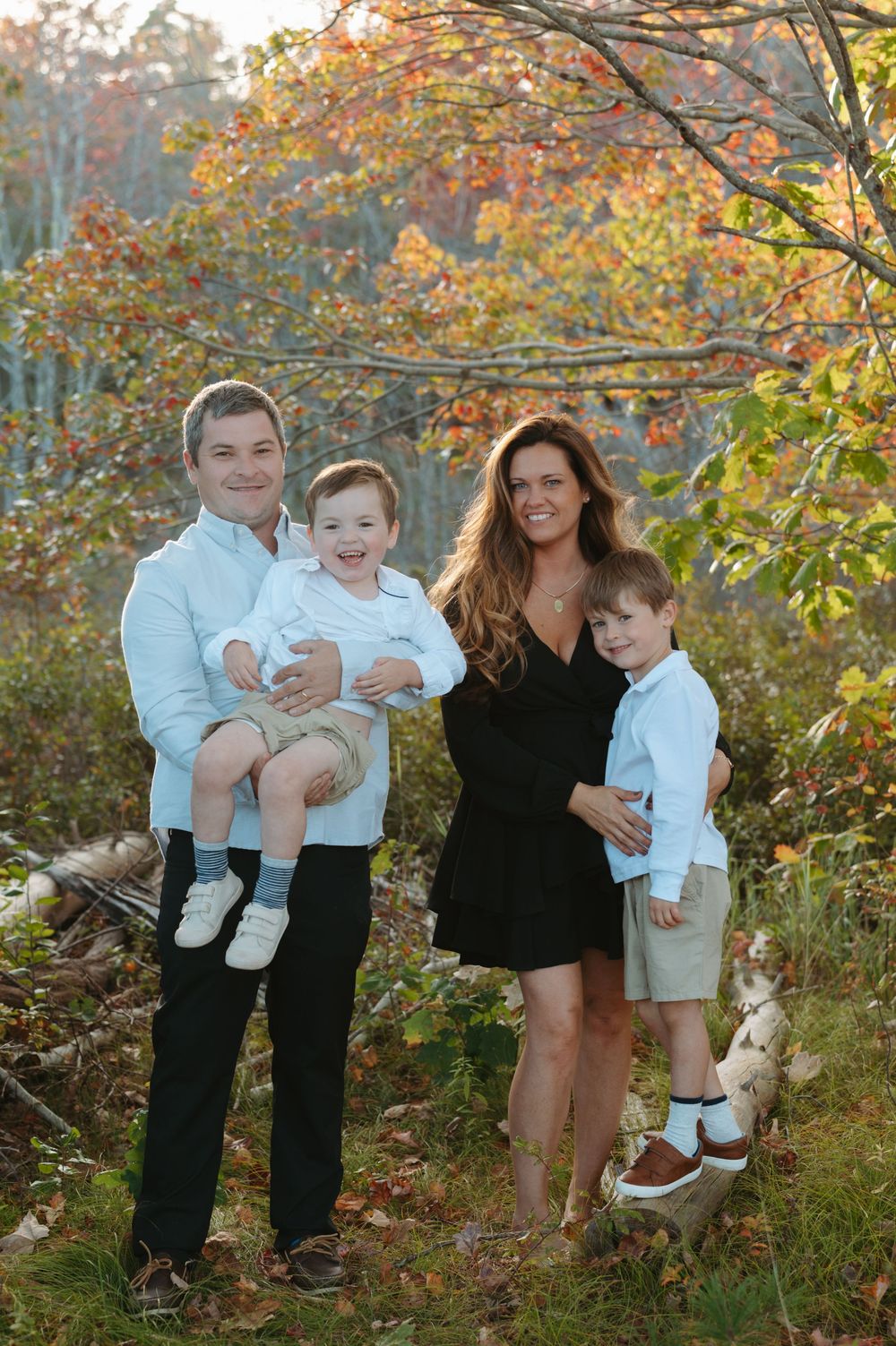 A family group poses together outdoors among colorful fall trees and foliage.