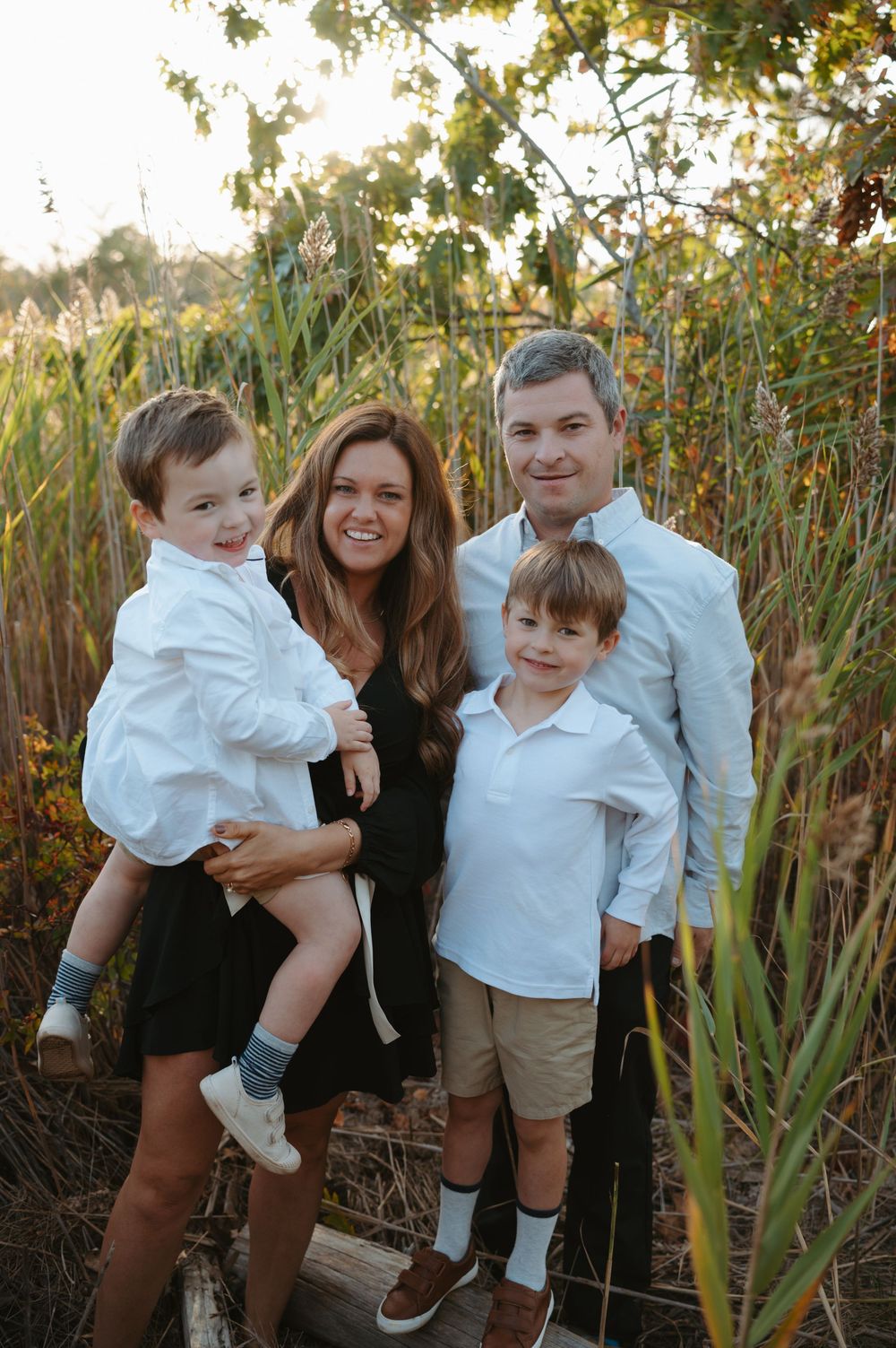 Family enjoying candid moments together outdoors among tall reeds during golden hour.