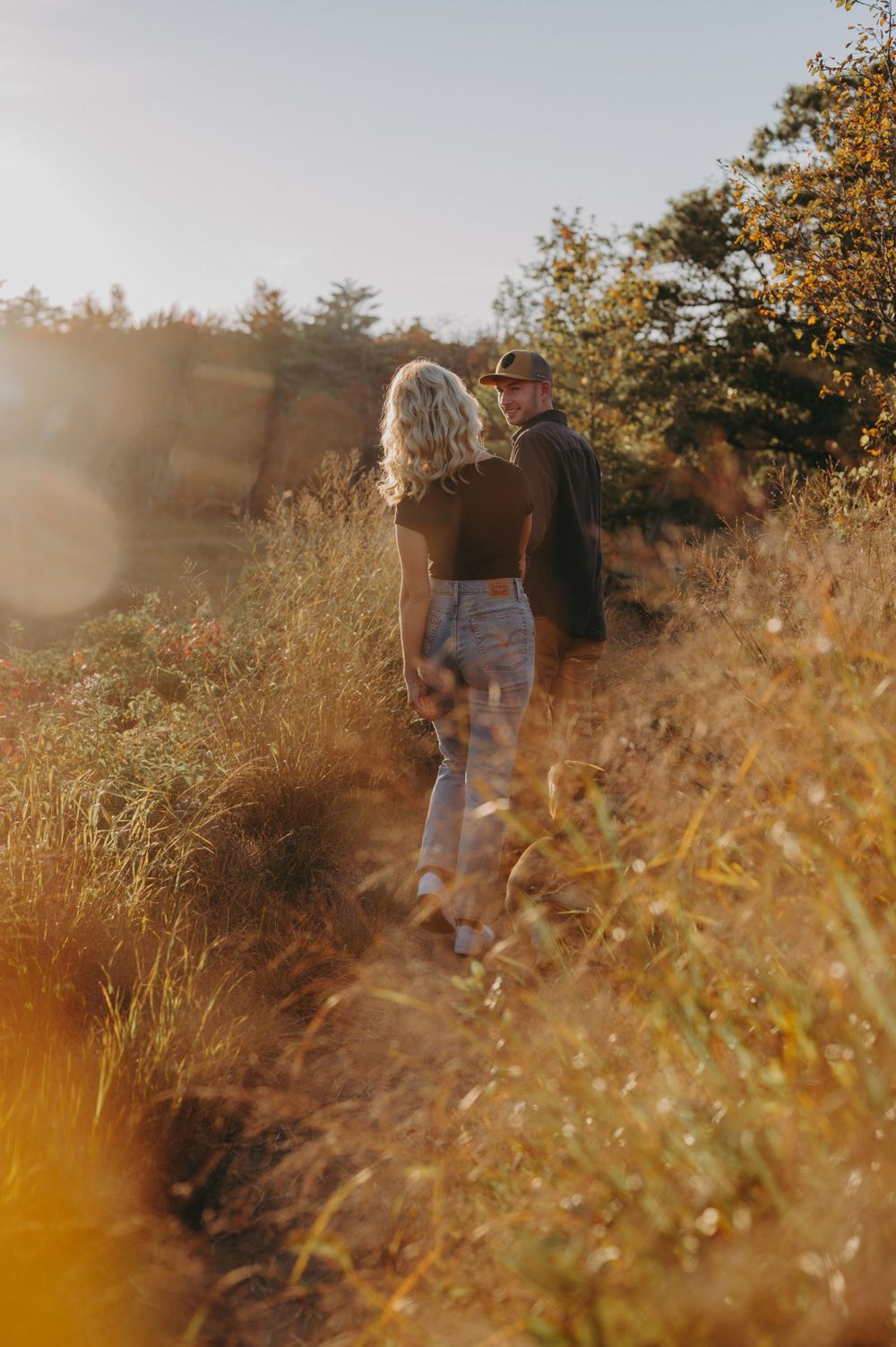 Couple walking through golden autumn field at sunset with magical lens flare.