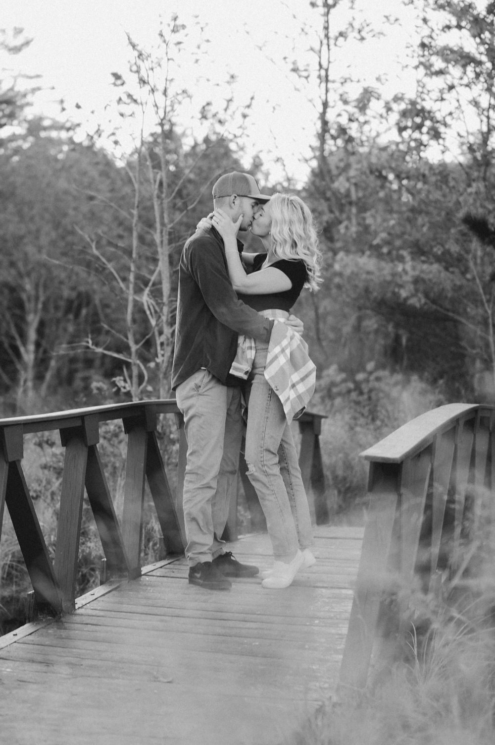 A romantic black and white photo of a couple embracing on a wooden footbridge.