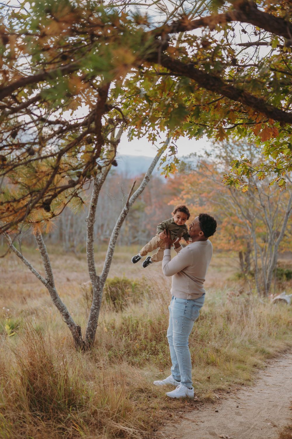 A touching autumn moment as someone lifts a small child among fall trees.