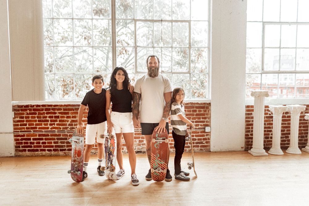 A family of four posing with skateboards in a studio, smiling and playful, with a modern backdrop and vibrant, energetic vibes.