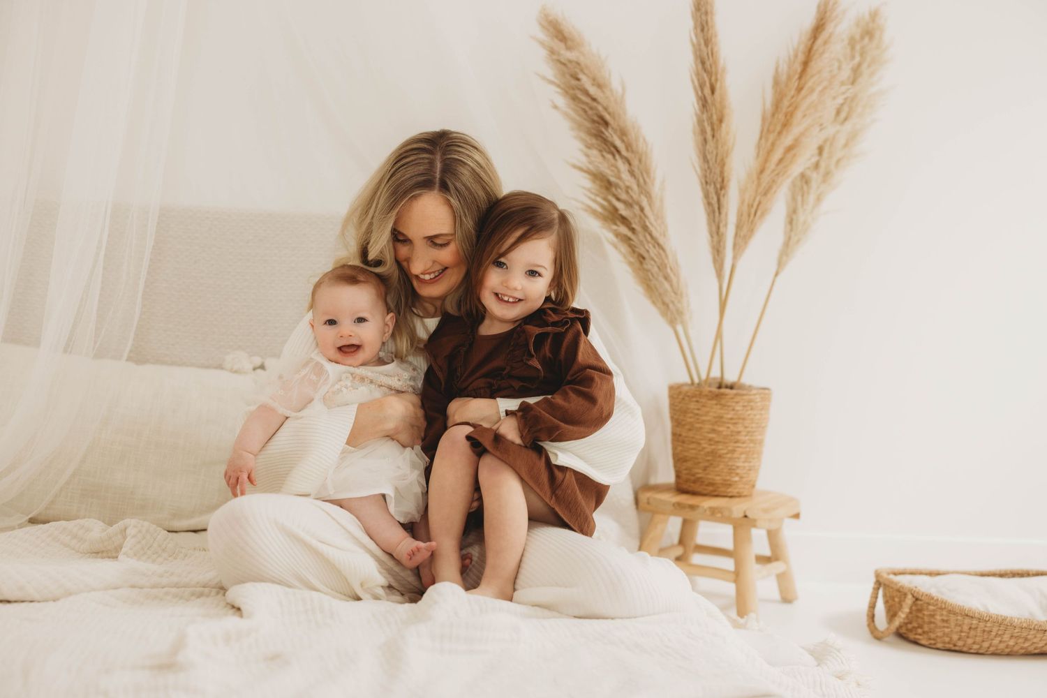 A peaceful family portrait in warm neutral tones with pampas grass decor on a light-colored bed.