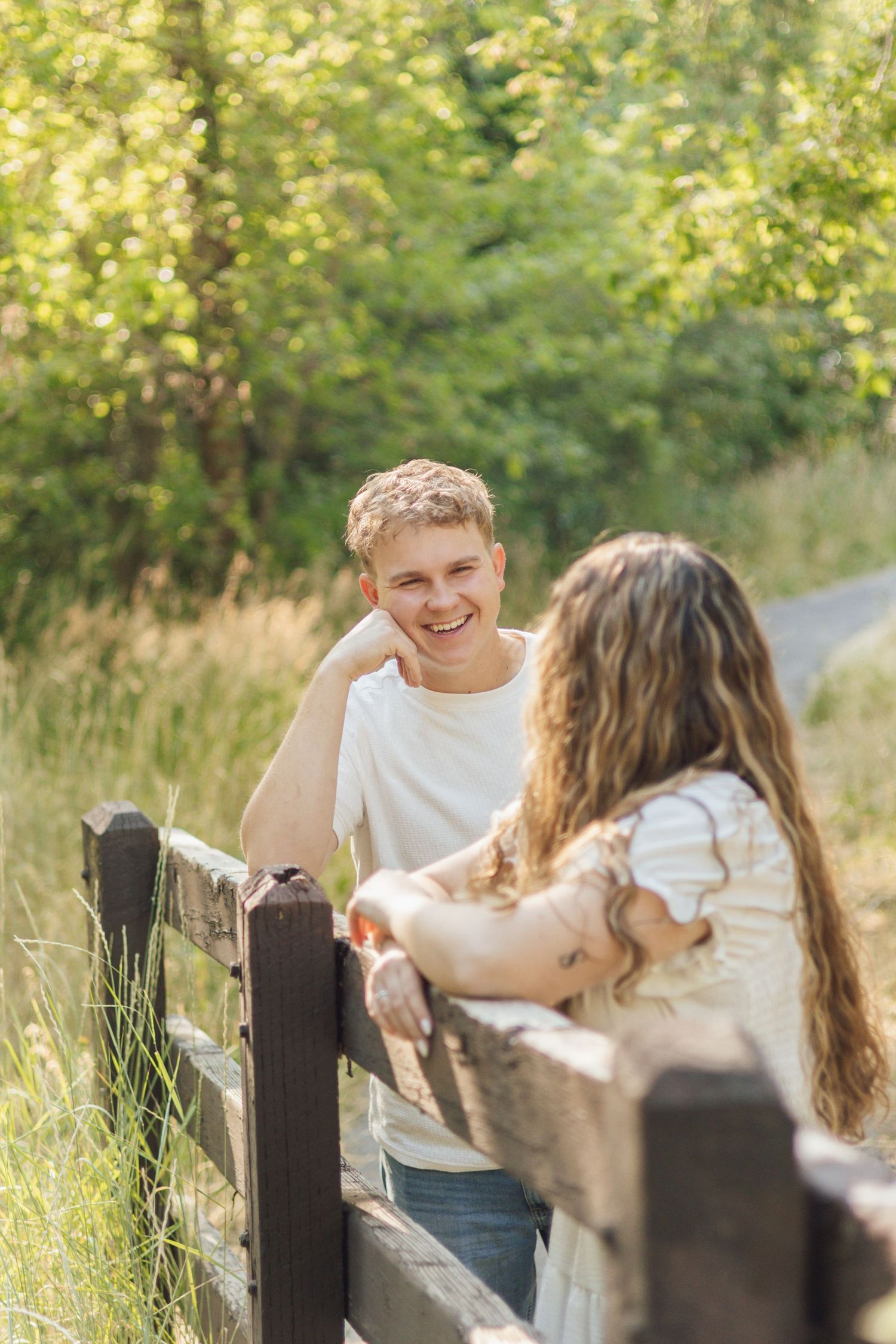 Couple standing beside a wooden fence, groom looking at his fiancée