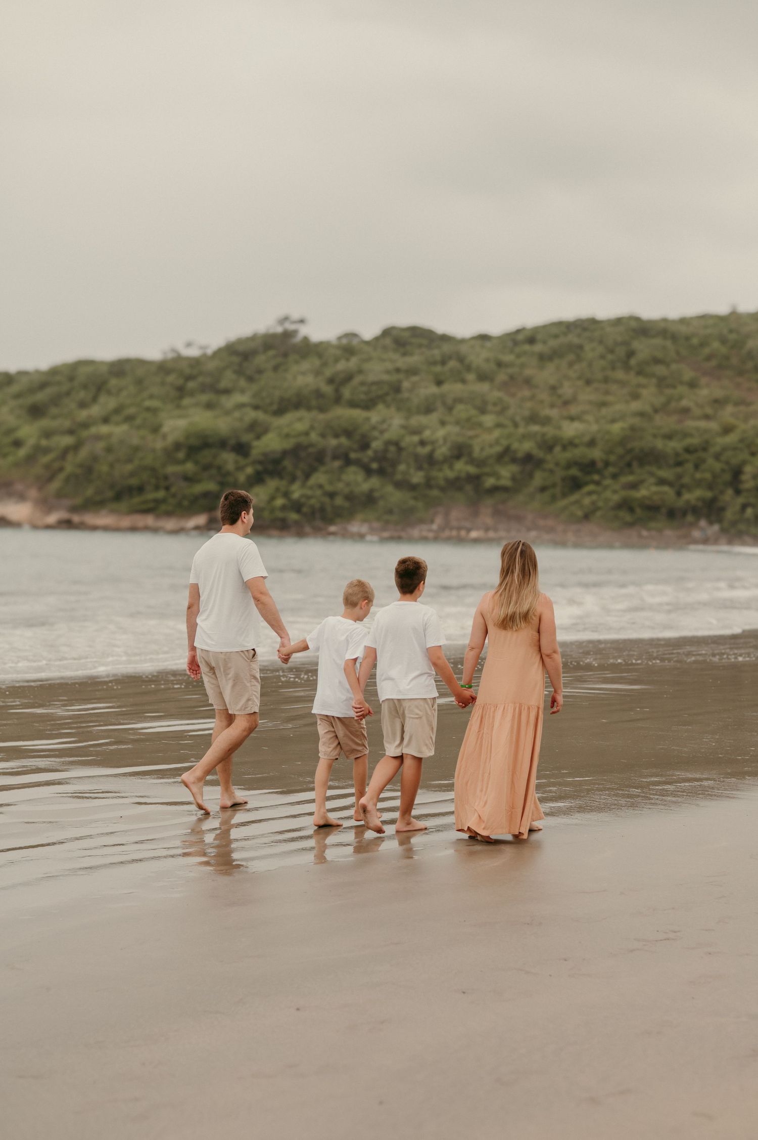 Family walking together on a beach shoreline during sunset with hills in the background.