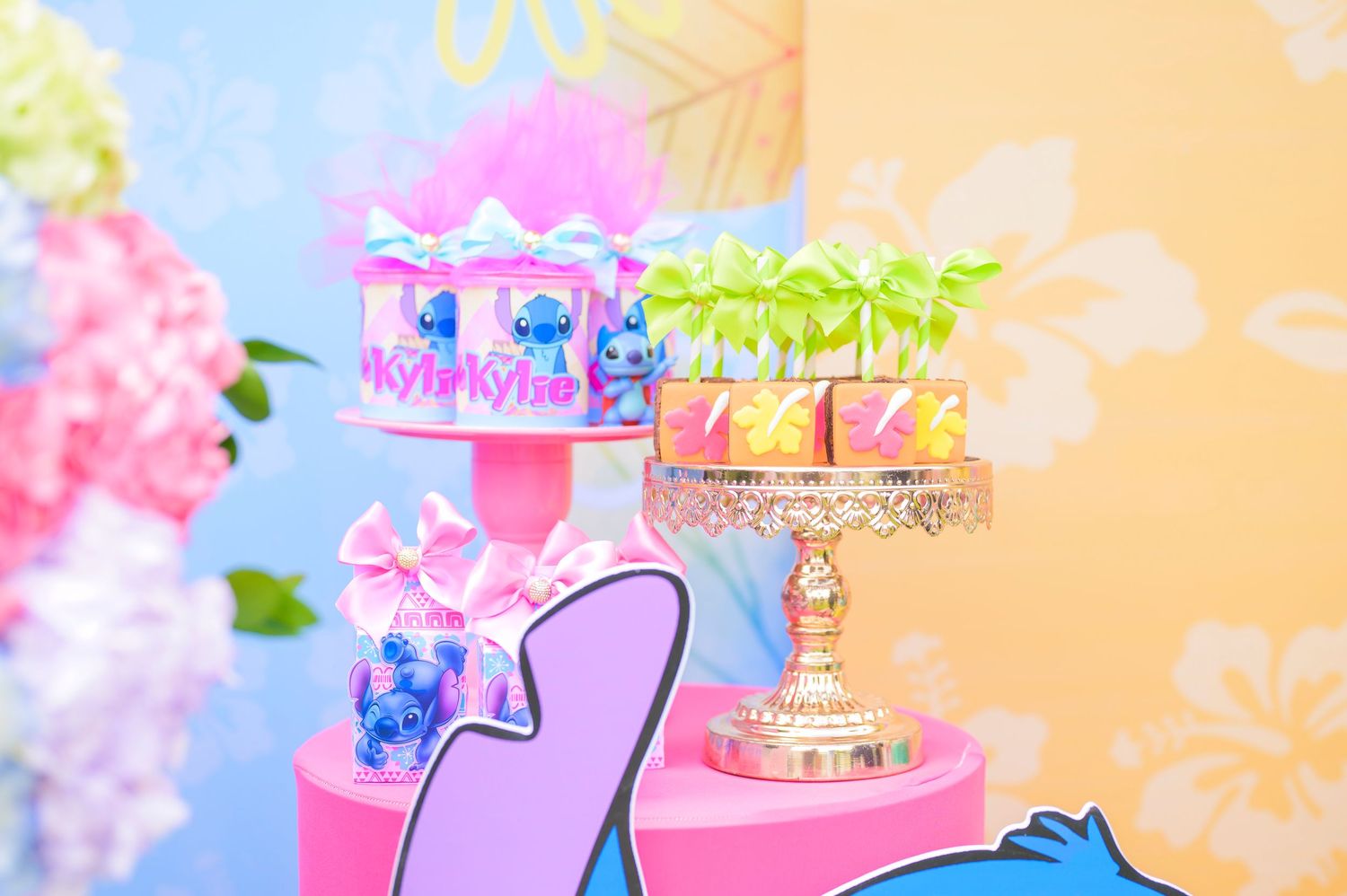 Colorful cake stands displayed on pink platforms with delicate floral decorations in the background.