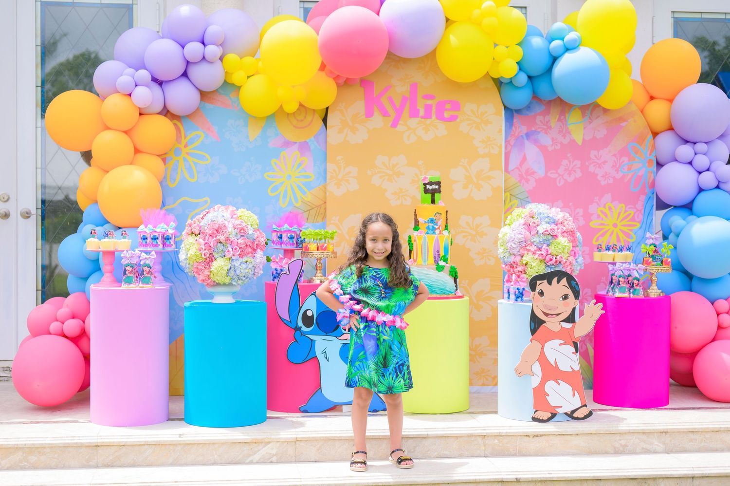 Colorful balloon arch with pastel decorations and party displays featuring an anime character theme and bright cylindrical stands.