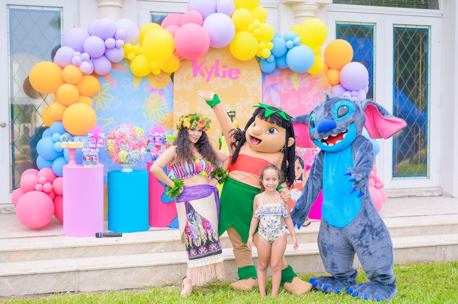 A little girl at her birthday party with Lilo and Stitch characters I front of colorful balloon arch displays at an outdoor party setup.