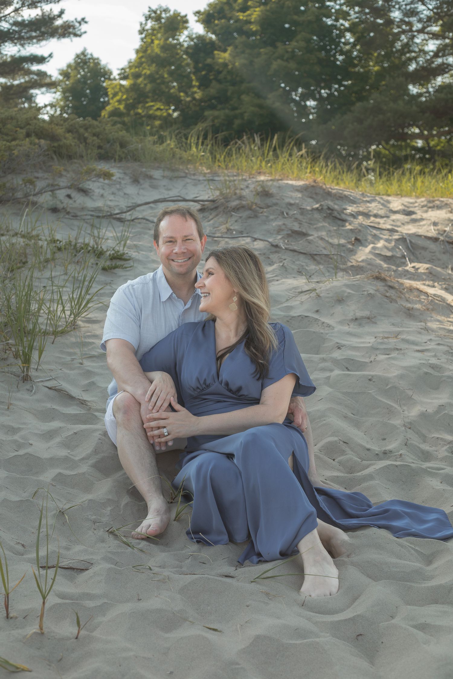 Couple sitting together on sandy beach dunes at sunset.