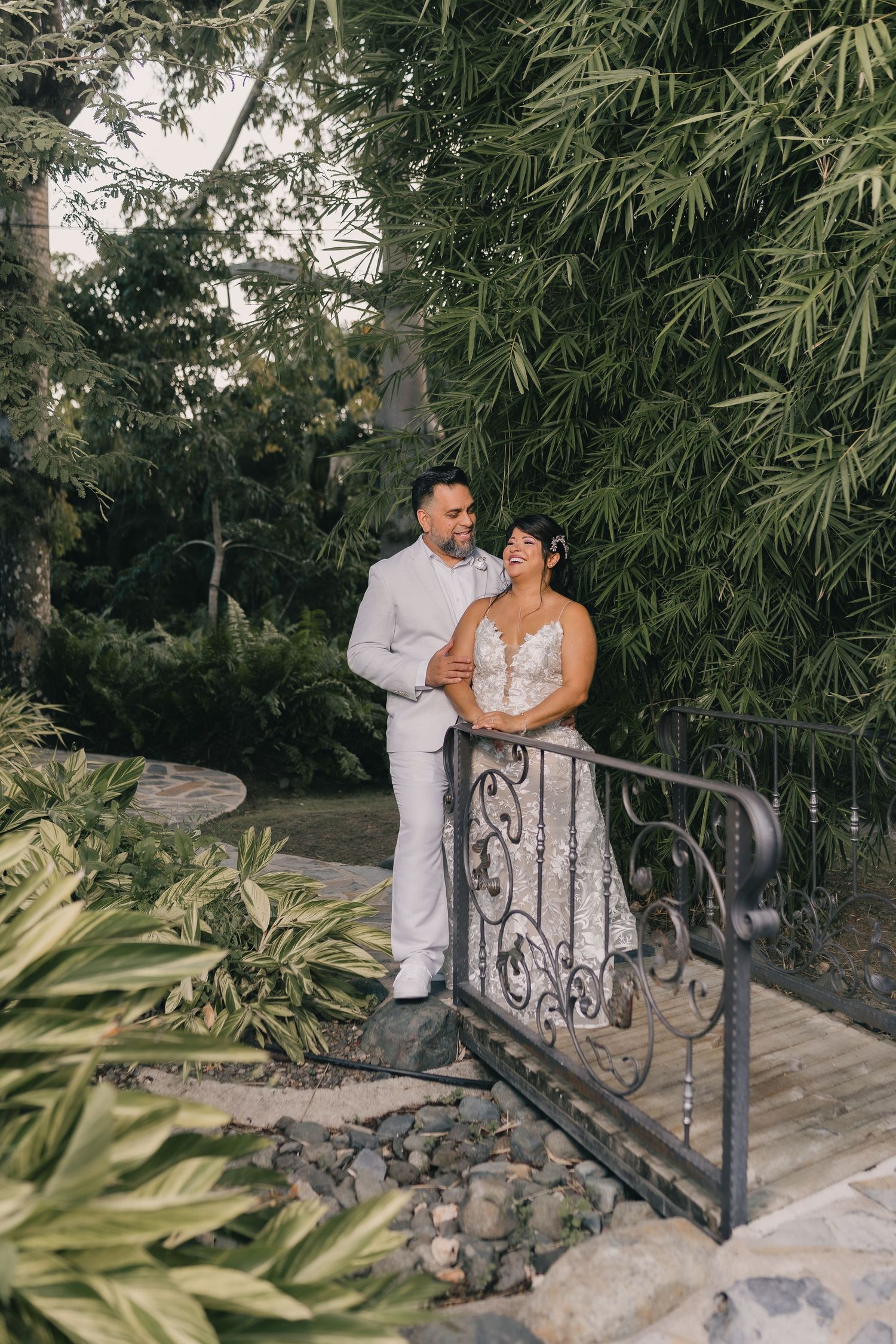 A couple shares an intimate moment on a stone pathway surrounded by lush tropical bamboo and plants.