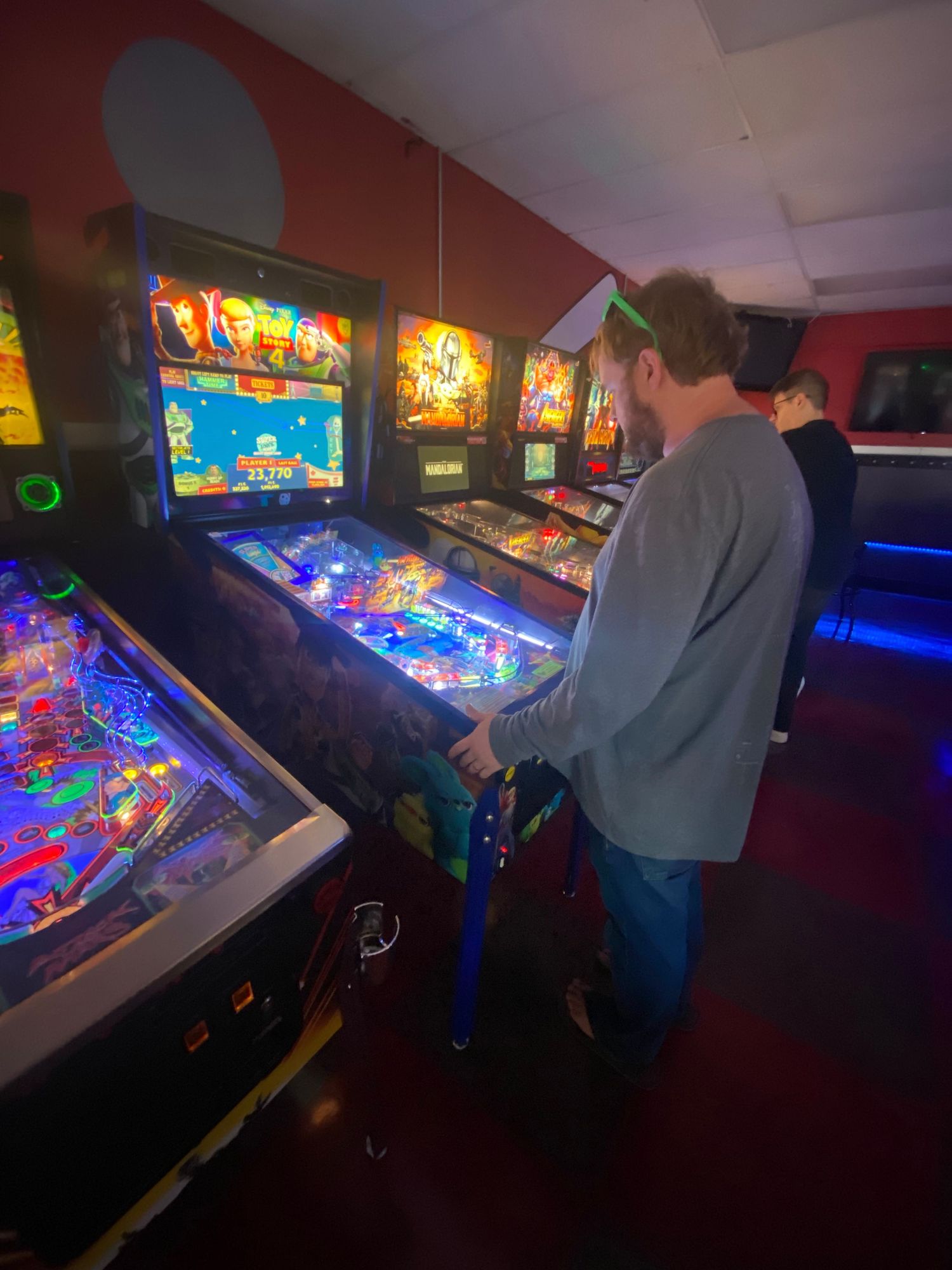 Colorfully lit pinball machines in arcade room with players enjoying classic games.