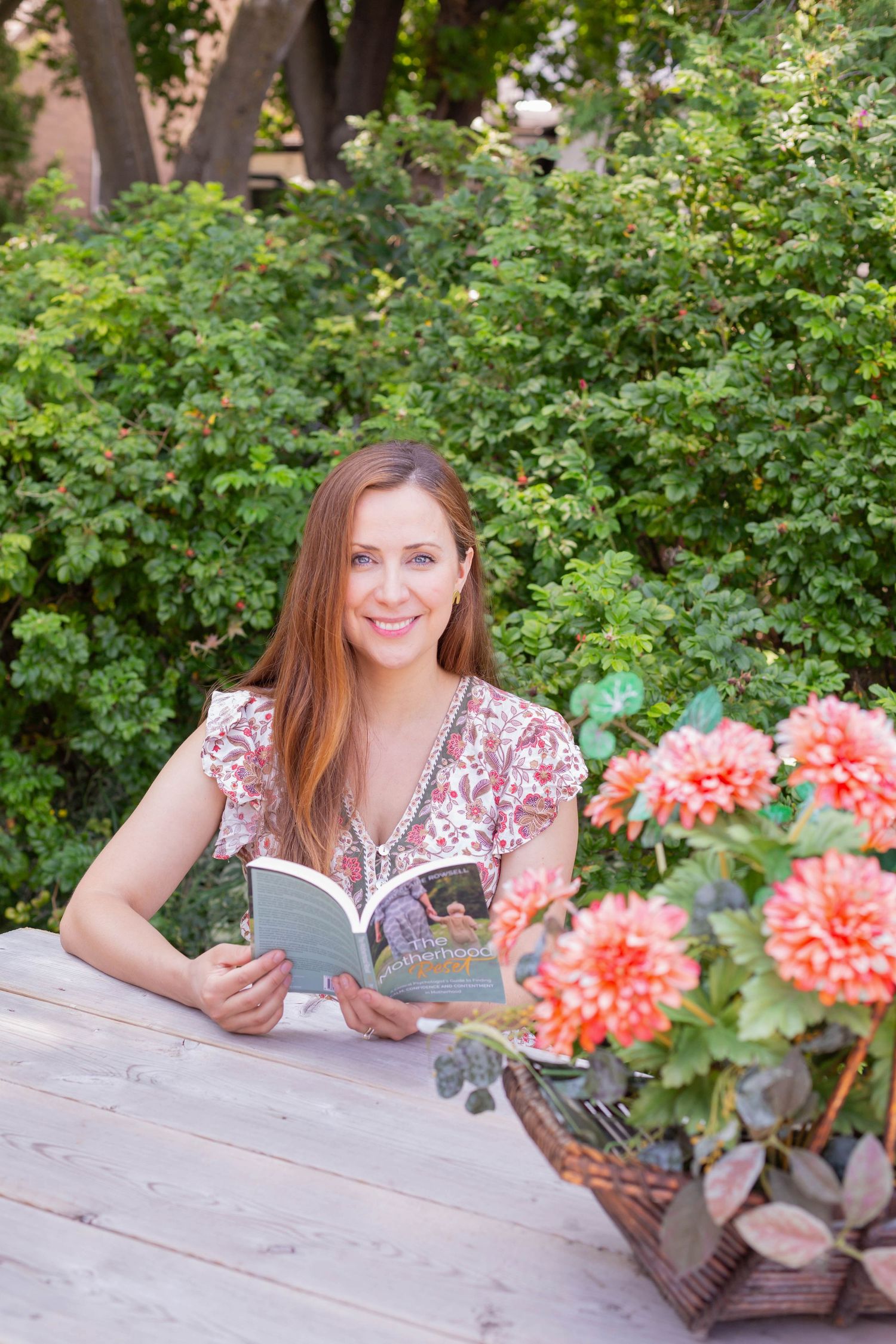 Reader enjoys book in garden setting surrounded by blooming dahlias and greenery.