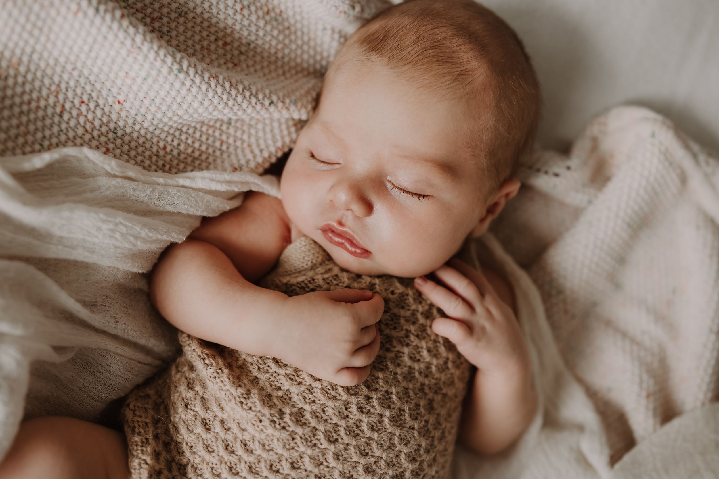 Close-up of newborn sleeping peacefully on a cream knit blanket during an in-home session. Westport NZ