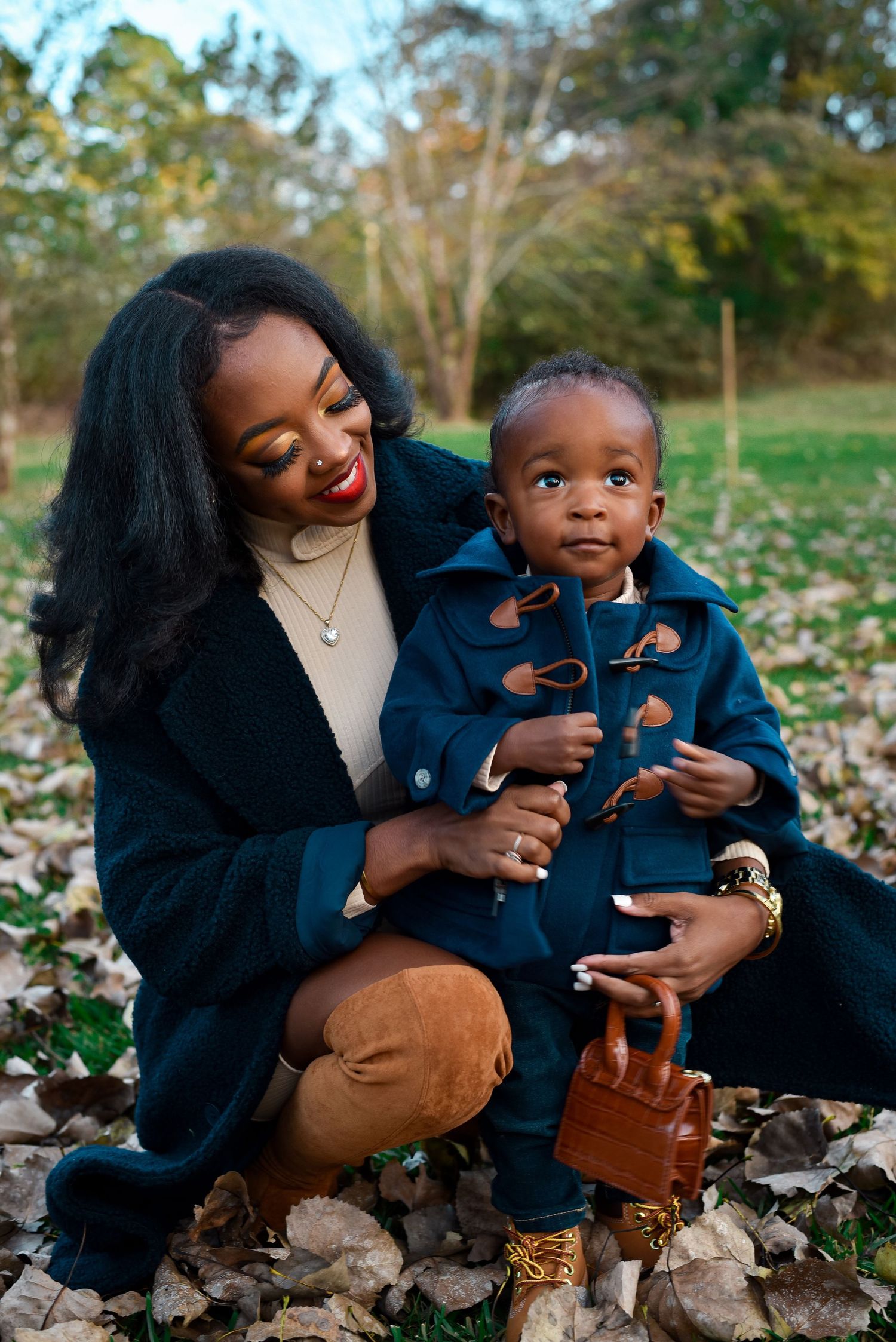 Parent and child share tender moments while sitting among autumn leaves in matching navy outfits.