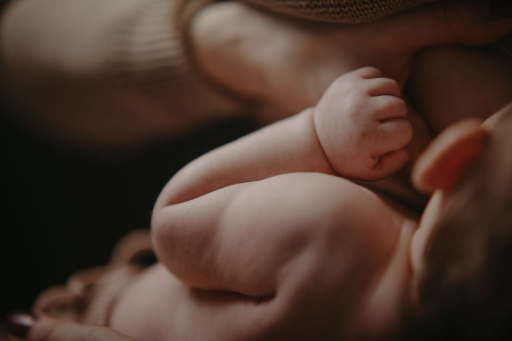 Close-up of a newborn baby's tiny feet and chubby legs resting on a mother's chest during skin-to-skin bonding.