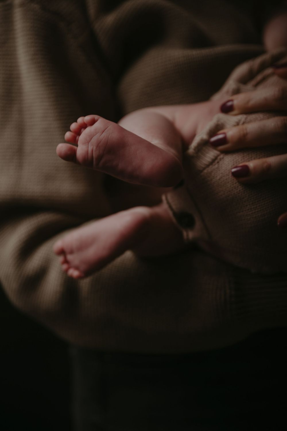Close-up of a newborn baby's tiny feet cradled in a mother's hands with dark red nail polish.