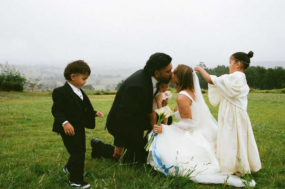 Wedding party gathers in a scenic green field with mountains in the background on an overcast day.