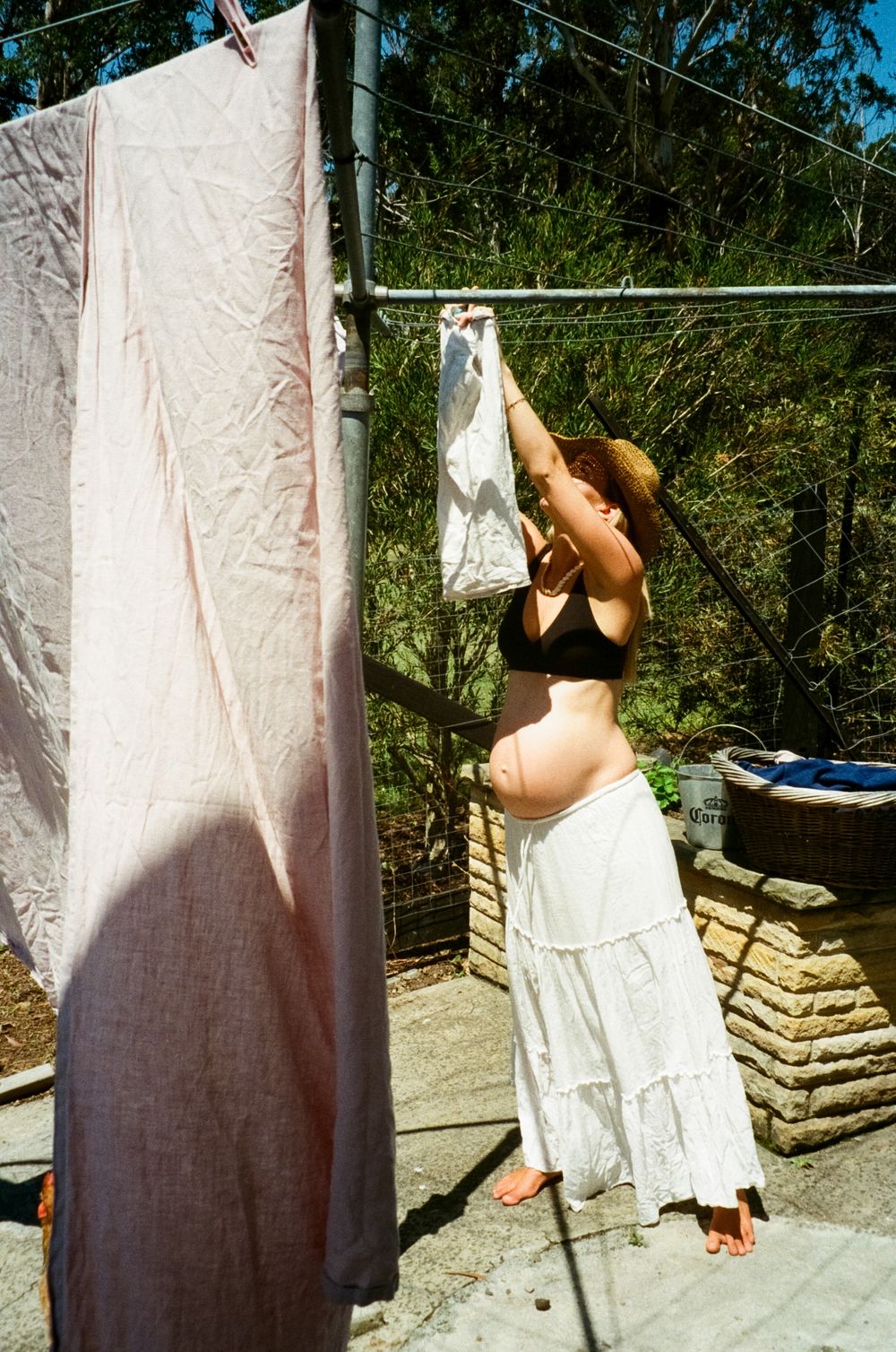 Someone hanging laundry on a clothesline on a sunny day, wearing a long white skirt and dark top.