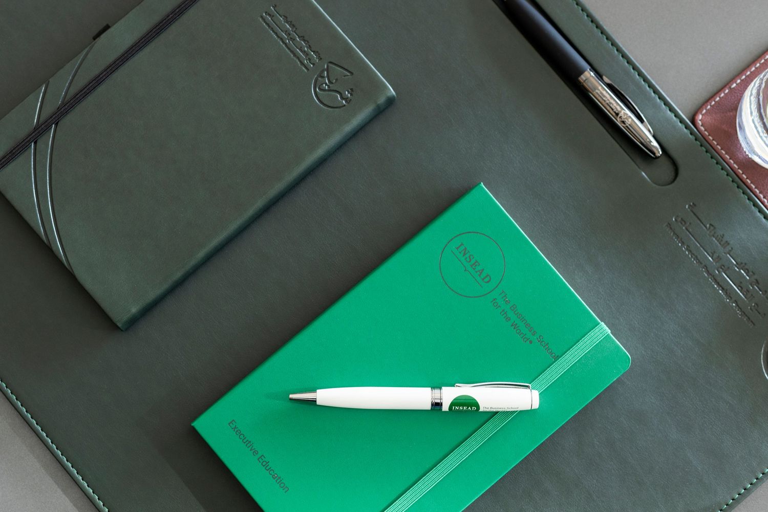 Two notebooks in gray and bright green colors with white pens lying on a dark surface.