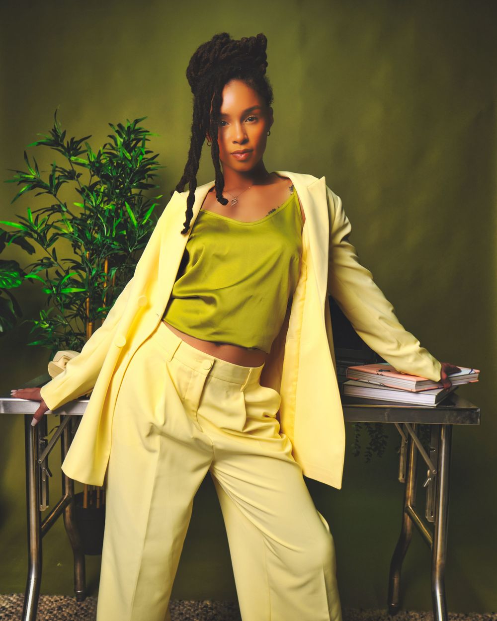 Stylish fashion portrait with yellow blazer and pants ensemble against green botanical background.
