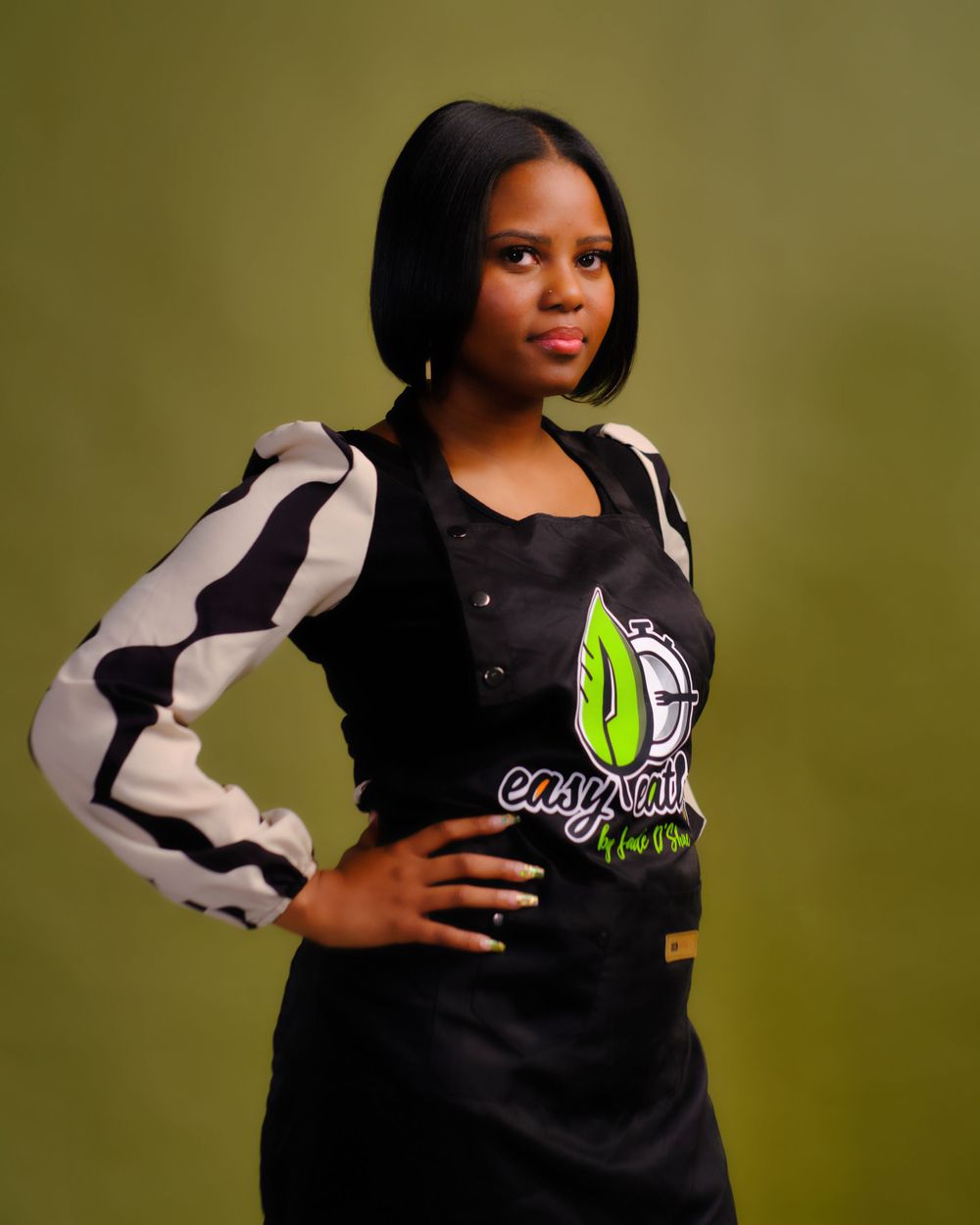 Person wearing black and white striped jacket with logo posing against olive green background.