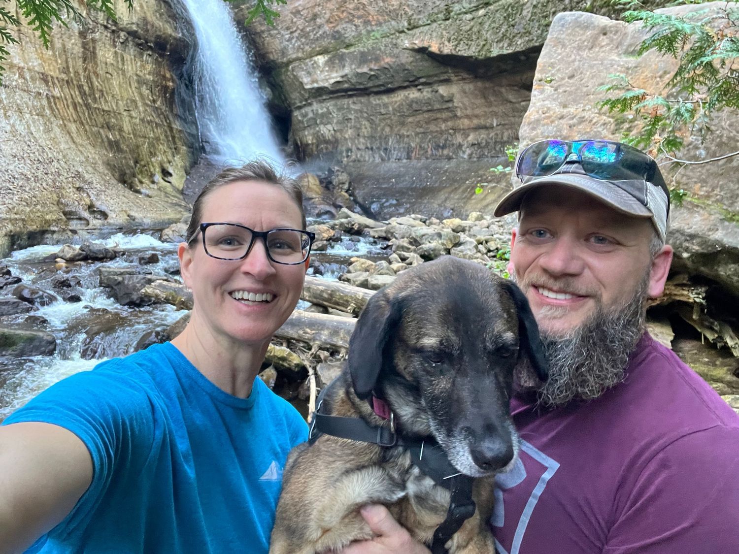Christina Newby hiking with her husband and dog near a waterfall during an outdoor adventure