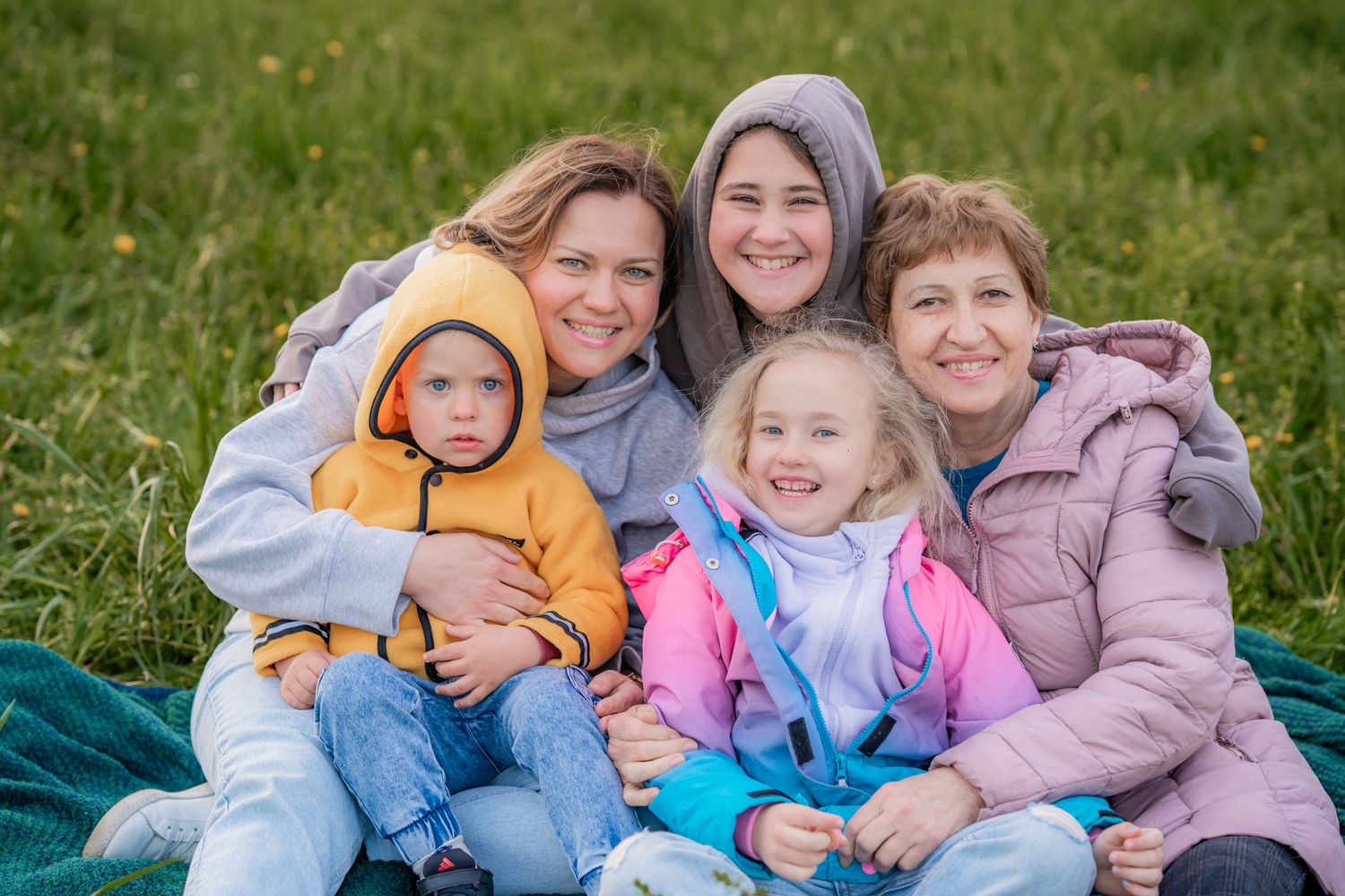 Group wearing cozy winter jackets sitting together on grass outdoors and smiling at camera.