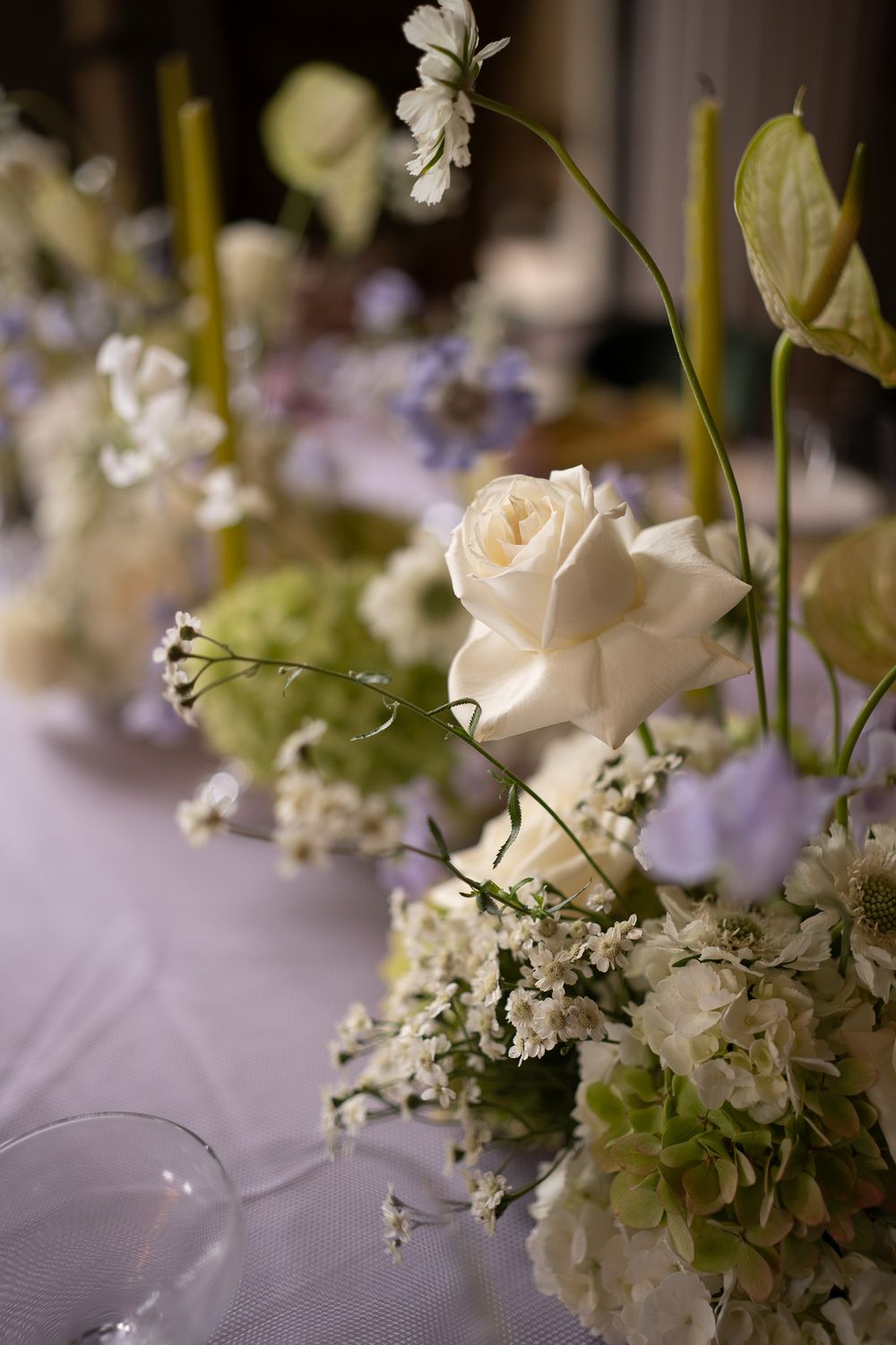 Elegant white roses and baby's breath arranged in a soft focus wedding centerpiece with delicate greenery on a tablecloth.