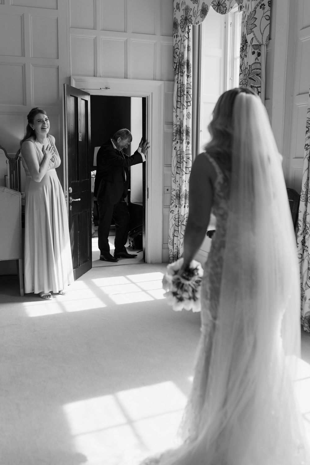 Black and white wedding scene showing reactions as the bride enters an elegant room.