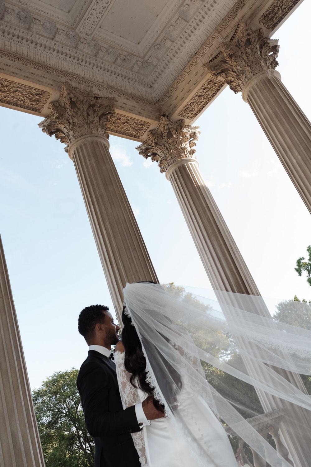 Wedding couple sharing intimate moment under ornate classical columns.