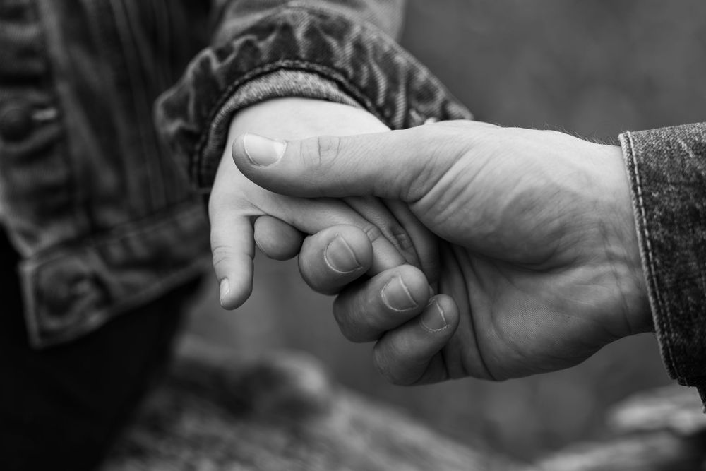 Black and white photo of an adult holding a small child's hand, symbolizing love, trust, and family bond.