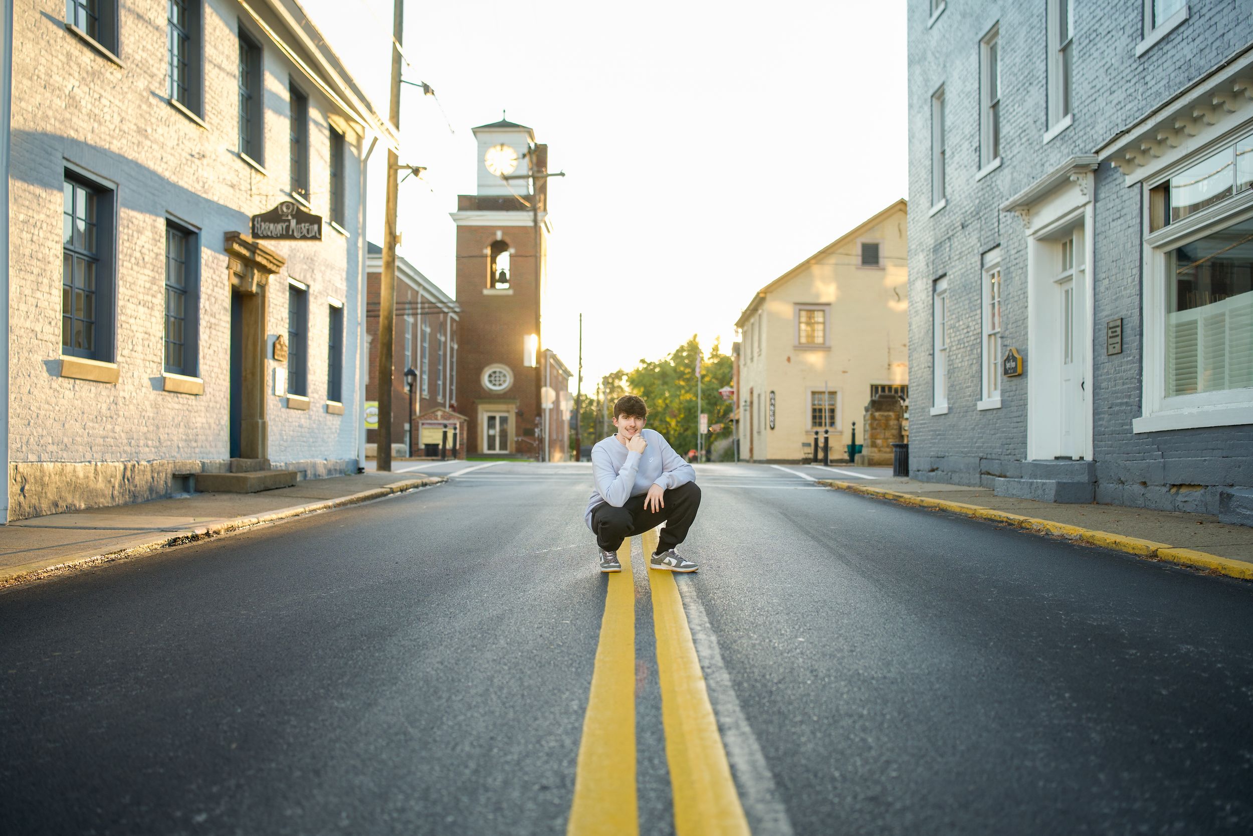 Young man crouching on yellow center line of empty small town street at golden hour.