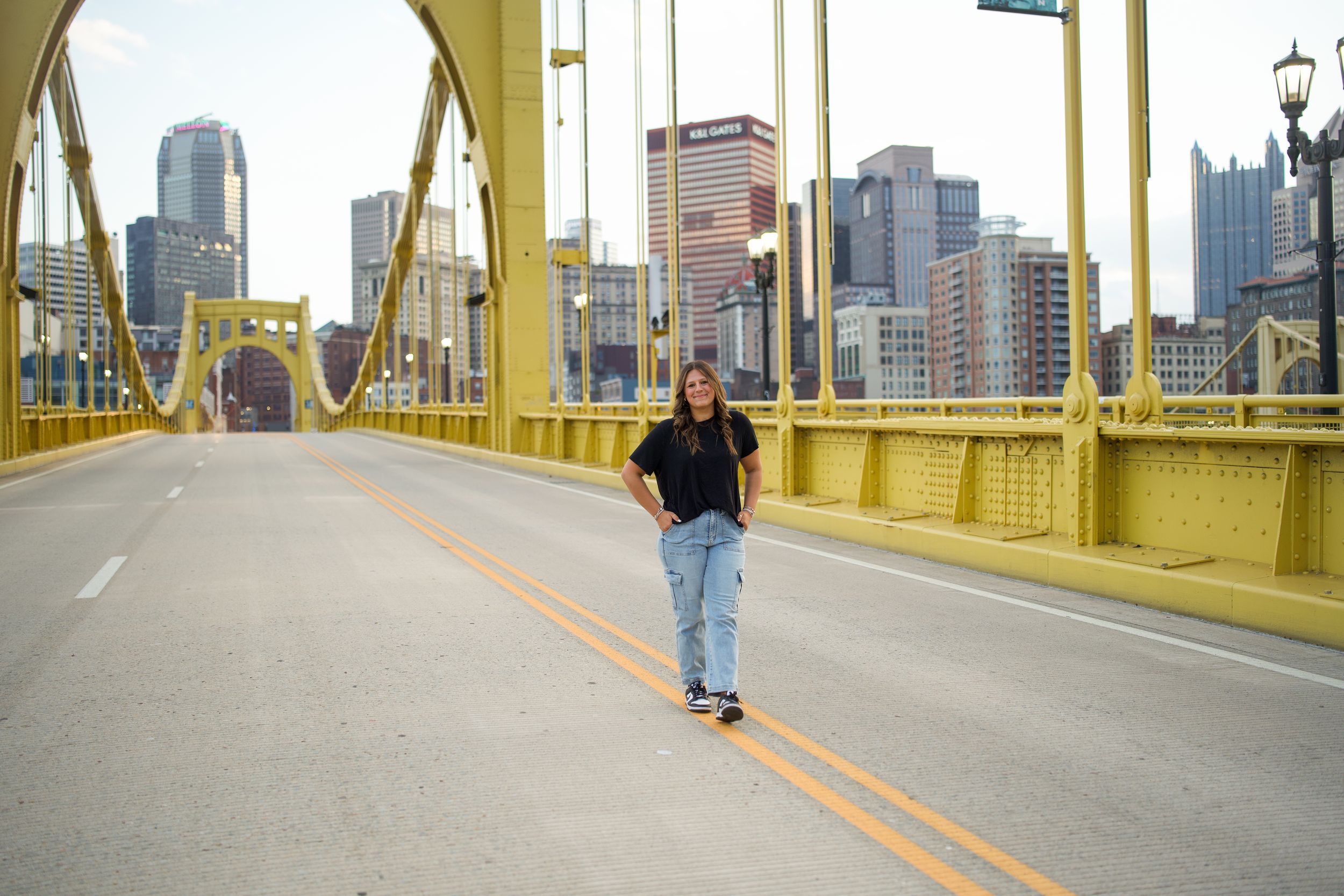 A person in blue jeans and dark jacket walks on the yellow Roberto Clemente Bridge in downtown Pittsburgh.