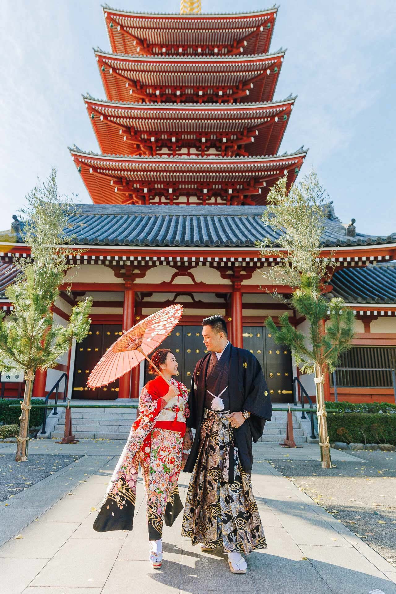 A couple in traditional Japanese attire poses with parasol in front of a five-story pagoda.