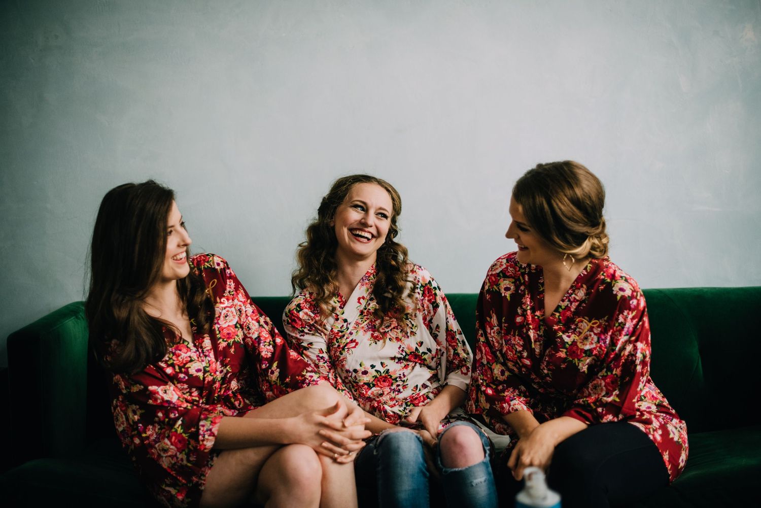 Jordan and her bridesmaids giggling together with stunning getting ready robes. Sitting on a dark velvet green couch.