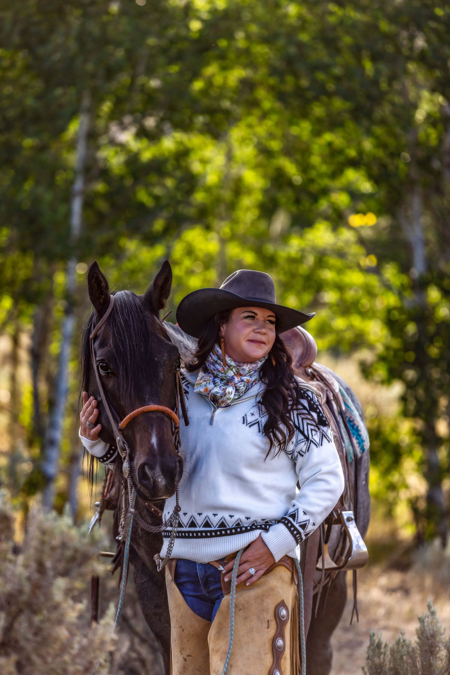 Equestrian with horse wearing western attire stands in autumn forest setting.