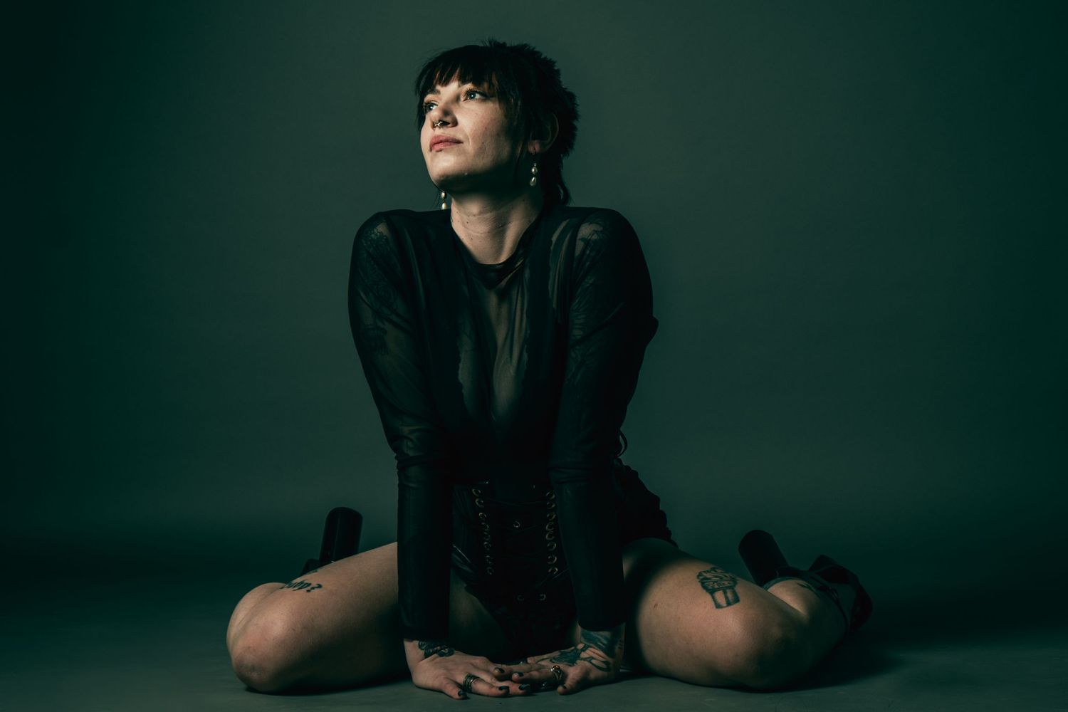 Dramatic pose in dark clothing against deep green studio background.