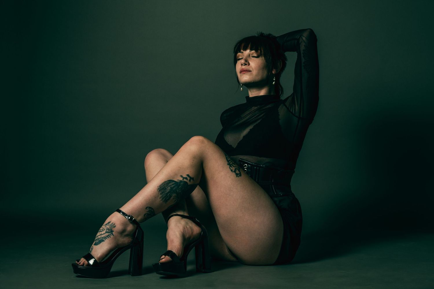 Dramatic studio portrait in black attire against dark green background.