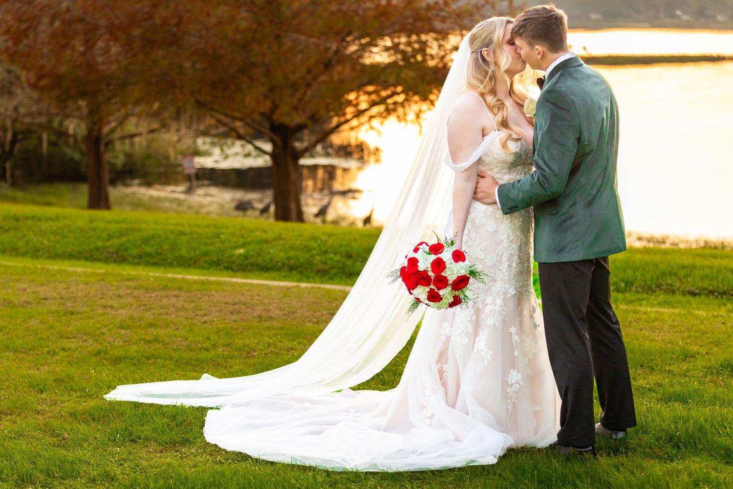 Wedding couple embraces outdoors at sunset with bride's long veil trailing behind. Lake Mary, Florida