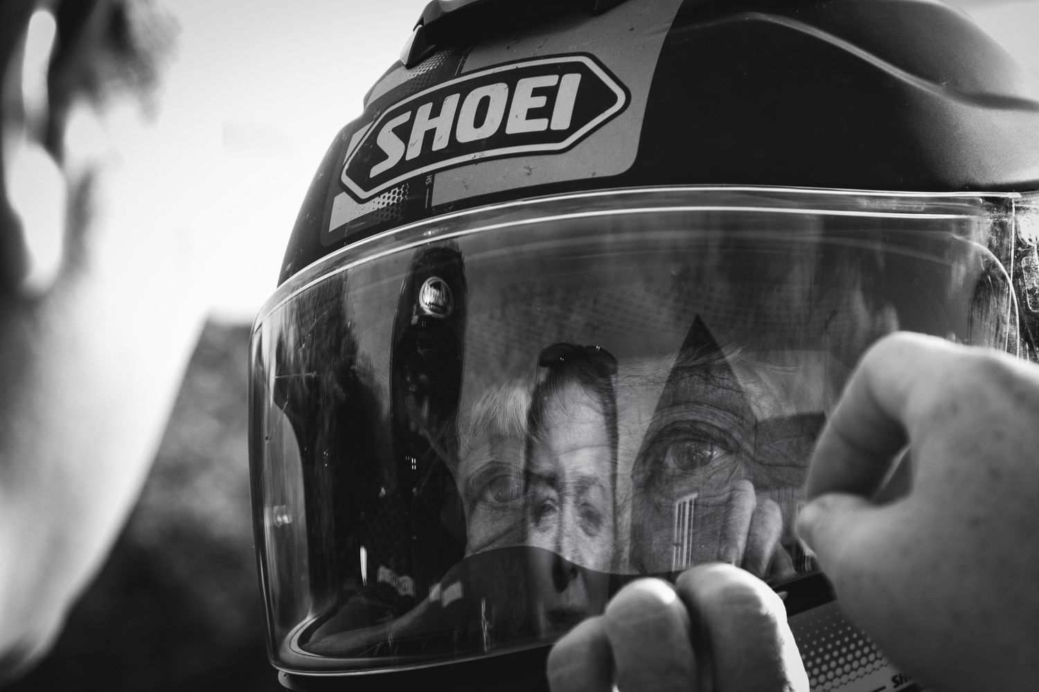 Black and white image of a motorcycle helmet with Shoei branding being adjusted.