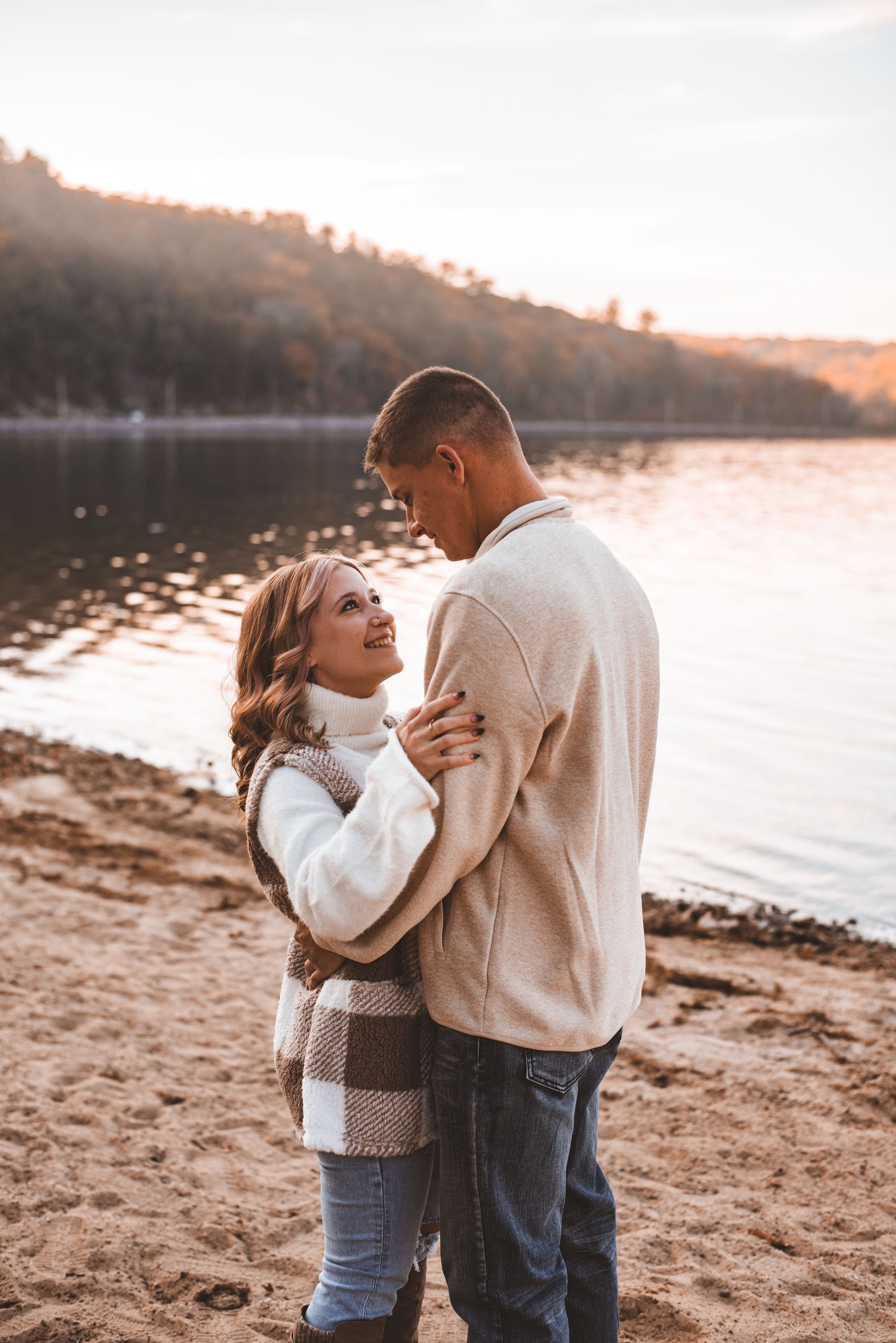 Romantic couple sharing an intimate moment on beach at sunset with lake and hills behind them.