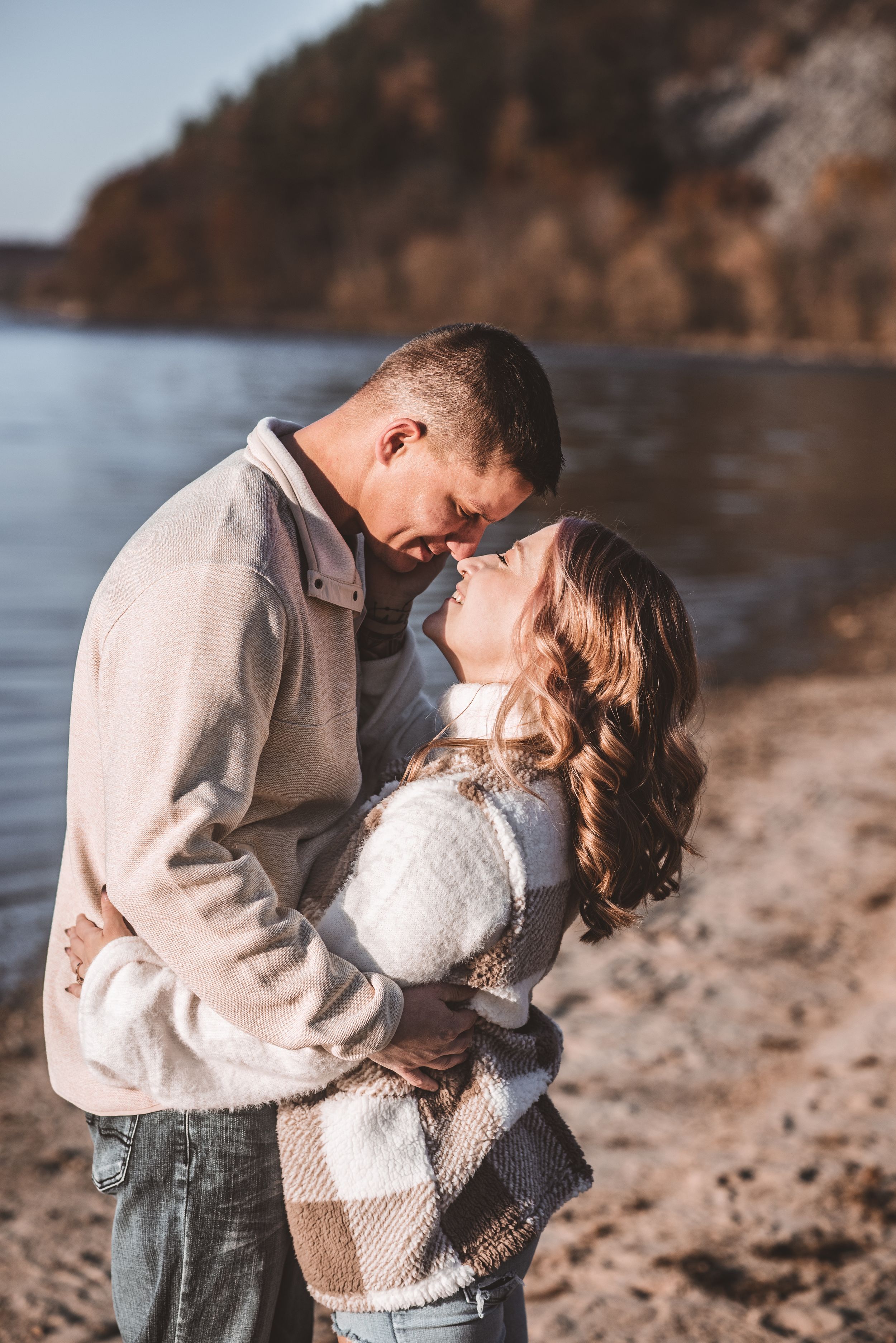 Intimate romantic moment shared on rocky beach with lake and cliffs in background.